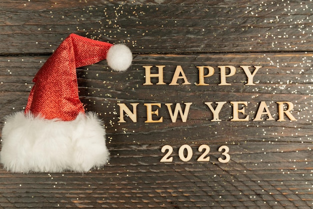 Festive greeting card for 2023 new year with red santa hat and wooden text on a table copy psace for text