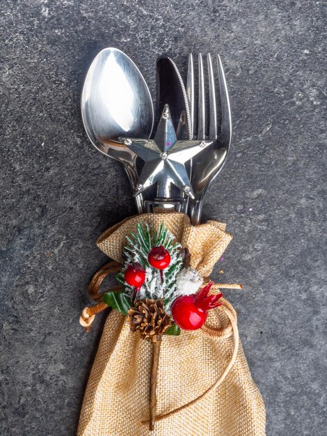 Festive Greeting Card Merry Christmas and Happy New Year Winter holiday dinner spoon fork knife in burlap decorated with rope star Christmas tree branch and berry cone on grey mabrle background