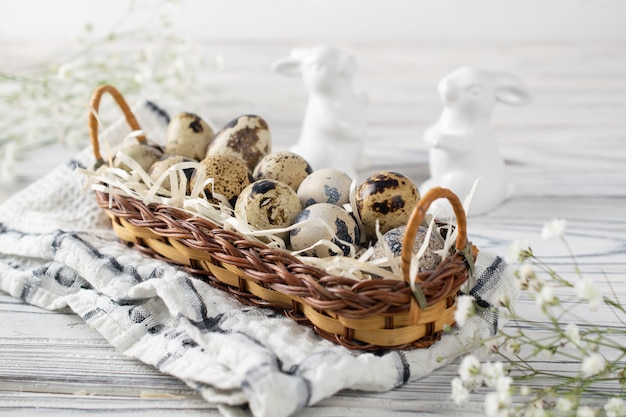 Festive happy easter decoration with quail eggs in a basket and ceramic bunnies