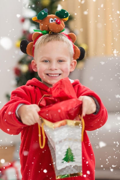 Festive little boy smiling at camera with gift against snow falling