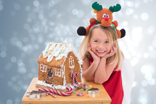 Photo festive little girl making gingerbread house against light design shimmering on silver