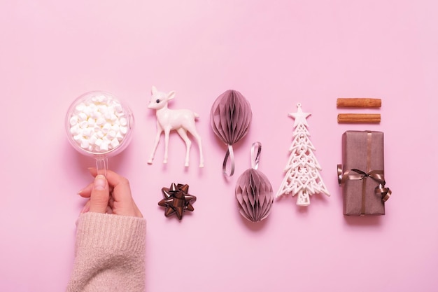 Festive minimal creative christmas composition with gifts paper balls and female hand with marsh mellow flat lay on pink background