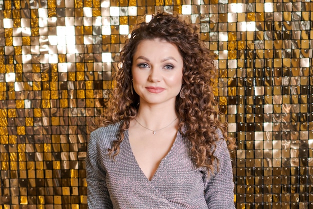 Festive mood in beautiful young woman on background shiny golden wall smiles