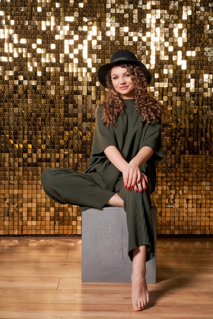 Festive mood in beautiful young woman on background shiny golden wall smiles