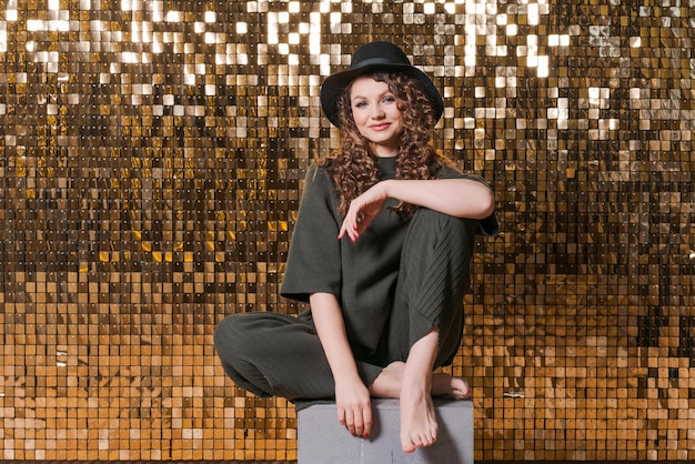 Festive mood in beautiful young woman on background shiny golden wall smiles