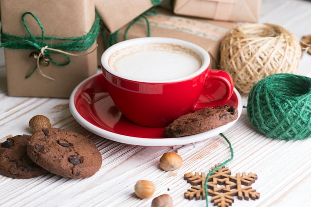 Festive mood. Gifts, cup cappuccino and Christmas decor on the wooden background.