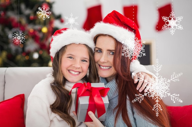 Festive mother and daughter holding christmas present against hanging snowflakes