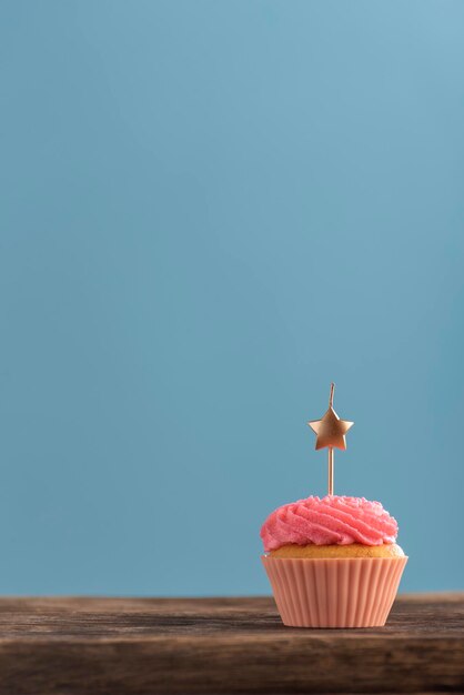 Photo festive muffin frosted with pink buttercream frosting with candle on pink background. vertical frame. copy space.