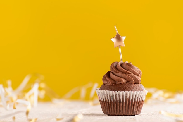 Festive muffin on yellow background. Chocolate cupcake with candles in the shape of star. Copy space.