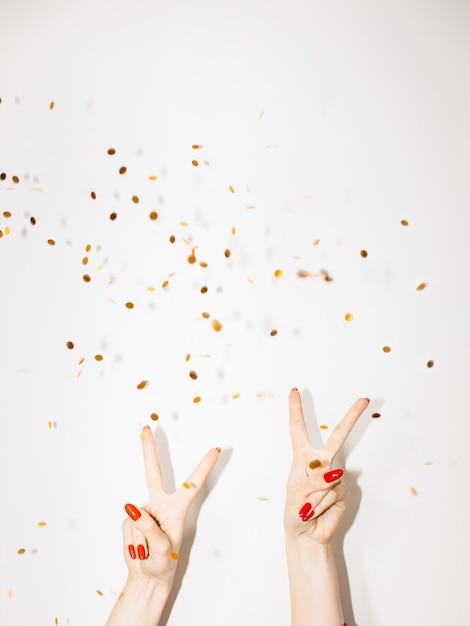 Photo festive party christmas background new year celebration female hands showing peace gesture with throwing golden confetti spangles isolated white copy space