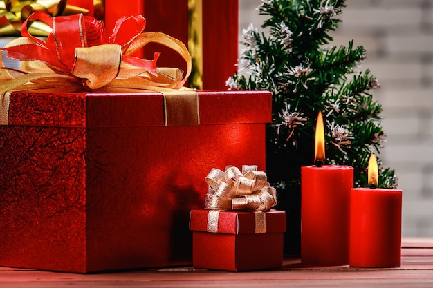 Festive red gift box and red lighten candles on natural wood board decorate with Christmas tree, Backgound of blurred white brick wall background.