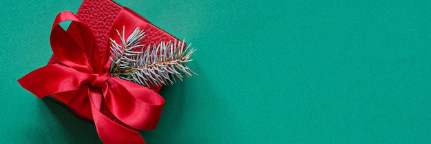 Festive red gift box with evergreen fir branches, on a green (emerald ) background. Christmas