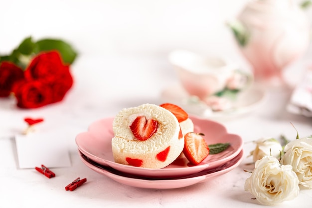 Festive roll with fresh strawberries and cream cheese on a white table and a bouquet of red roses Selective focus