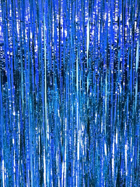 Photo festive shiny tinsel fringe, blue background with selective focus.