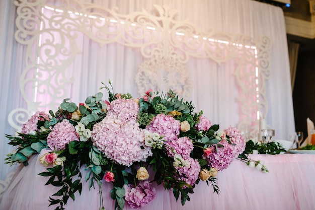 Festive table arch decorated with composition of violet purple pink flowers and greenery in the banquet hall Table newlyweds in the banquet area on wedding party