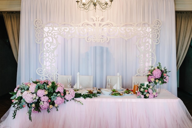 Festive table arch decorated with composition of violet purple pink flowers and greenery candles in the banquet hall Table newlyweds in the banquet area on wedding party