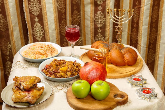 Festive table for a meal on Rosh Hashanah challah honey pomegranate apples wine and traditional chelnt and meat next to the menorah