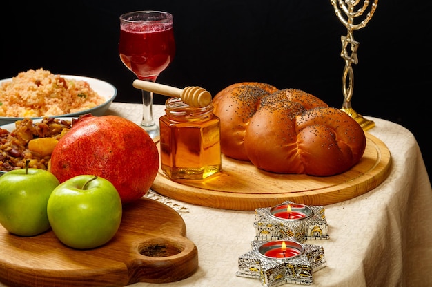 Festive table for a meal on Rosh Hashanah challah honey pomegranate apples wine and traditional chelnt