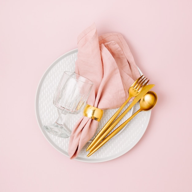 Festive table setting. Plates and cutlery with  pink napkin on white background. Beautiful flat lay arrangement.