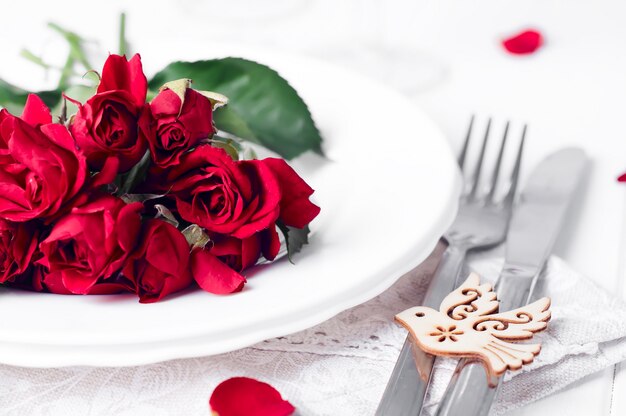 Festive table setting with beige roses, wine glasses, napkins and cutlery