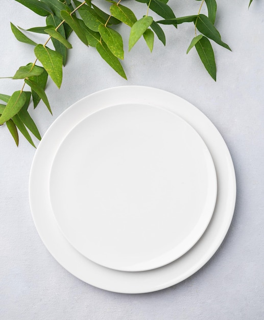 Festive table setting with white plates on a light background with eucalyptus branches