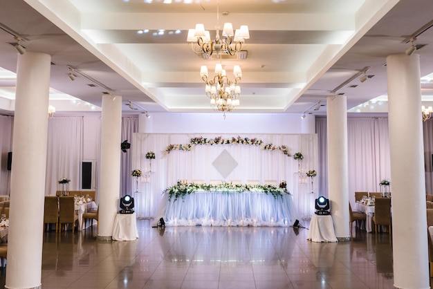 Festive table with arch decorated composition of white flowers and greenery in the banquet hall Table newlyweds and guests in the banquet area on wedding party