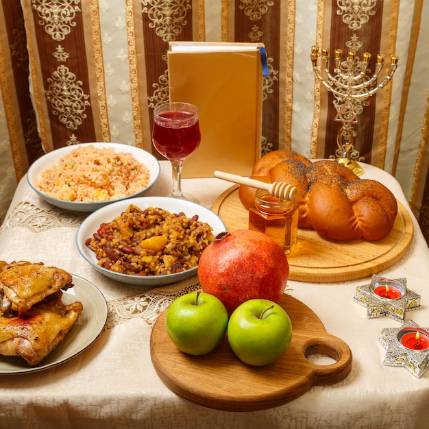 Festive table with ritual traditional dishes and menorah and siddur for Rosh Hashanah