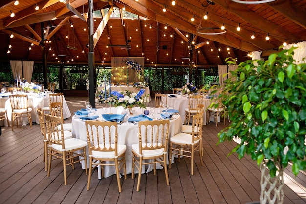 Festive wedding, table setting with blue linen napkins, candles, golden chairs, and fresh bouquets of flowers. Wedding decorations. Restaurant menu concept. Soft selective focus.