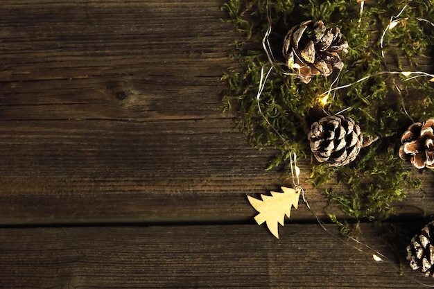 Festive wooden background with little wooden christmas tree, original cones and moss on it