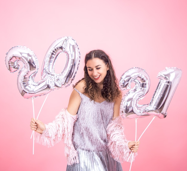 Festively dressed young girl cute smiling on a pink wall with silver balloons for the new year concept