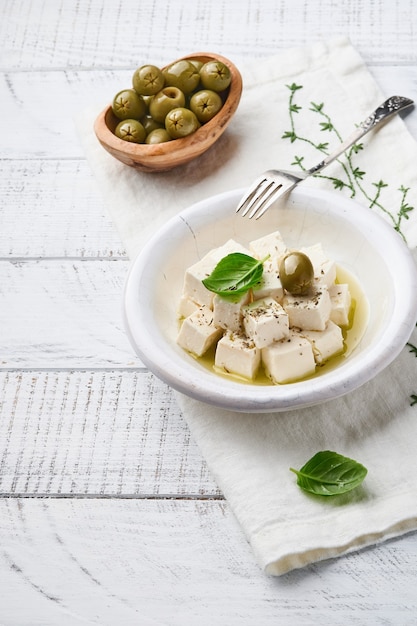 Feta cheese cubes with rosemary, olives and olive oil sauce in white bowl      