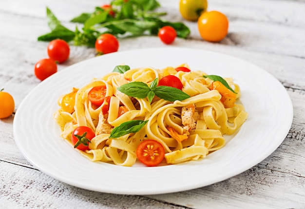 Fettuccine pasta in tomato sauce with chicken, tomatoes decorated with basil  table