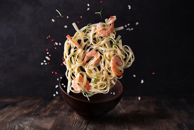 Fettuccine and prawns on dark wooden background levitating pasta with shrimps and spices