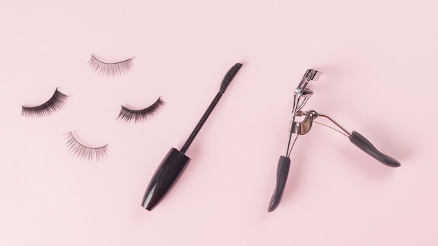 A few false eyelashes a brush and curlers on a pink background