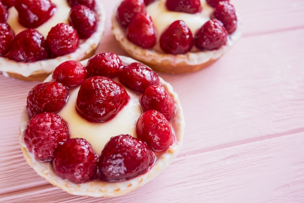 a few panna cotta pastries with cream and raspberries close up on a delicate pink wooden background with free space