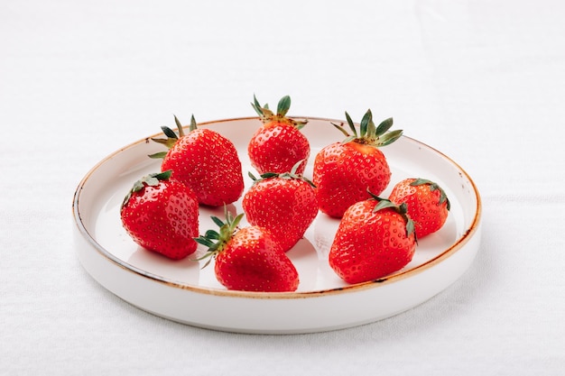 A few ripe juicy strawberries in a plate on a white background