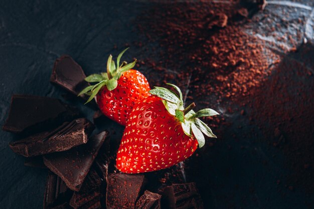 A few strawberries with chocolate and cocoa on a dark background