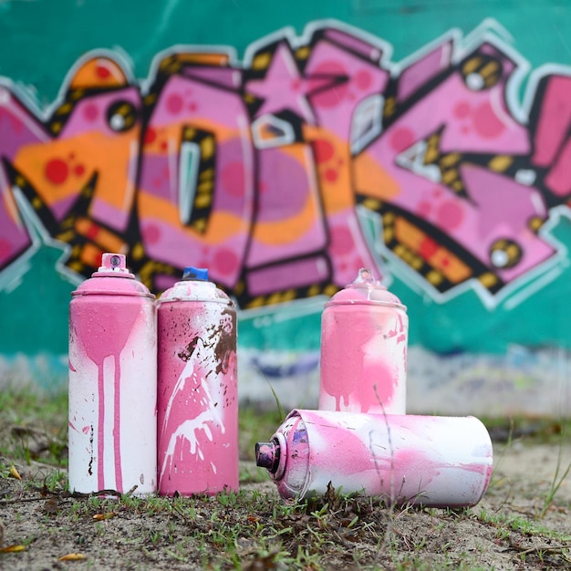 A few used paint cans lie on the ground near the wall with a beautiful graffiti painting in pink and green colors Street art concept