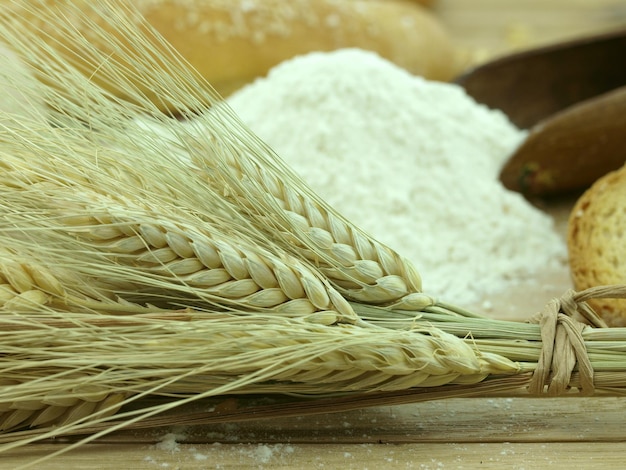 A few wheat ears are on a table with flours and bread.