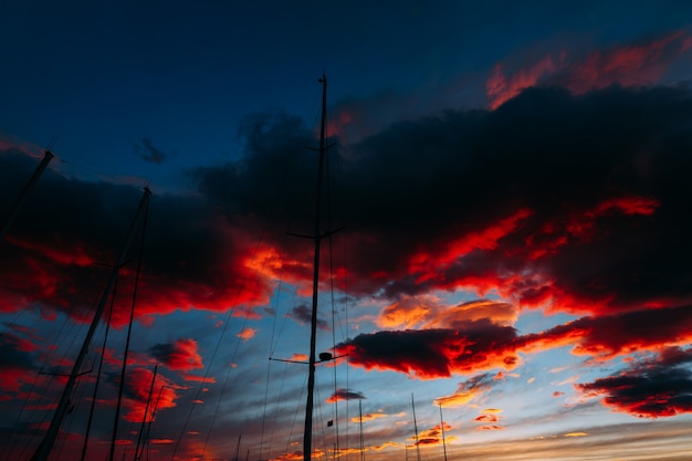 Fiery contrasting clouds in the blue sky at sunset through the masts of sailing yachts