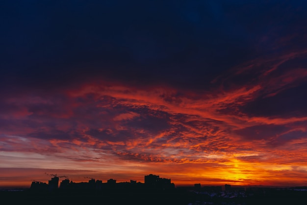 Fiery red blood vampire dawn. Amazing warm dramatic fire blue dark cloudy sky. Orange sunlight. Atmospheric background of sunrise in overcast weather. Hard cloudiness. Storm clouds warning. copyspace