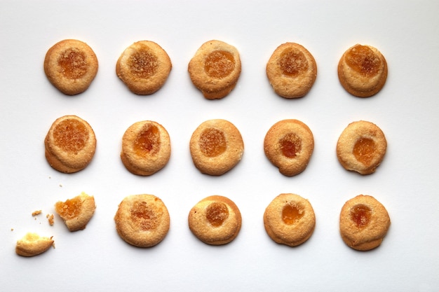 Fifteen handmade cookies with apricot jam arranged in even rows. One in the corner is broken. isolated on white background