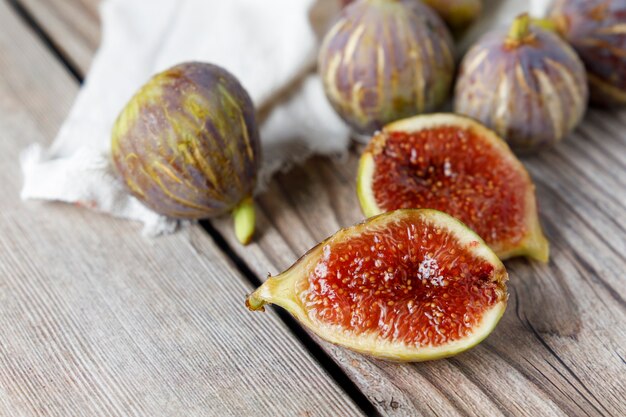 Fig open in two parts next to other whole figs on wooden table.