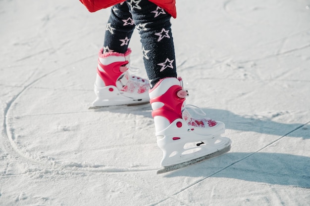 Figure skates on girl legs on the ice covered with snow and with traces made by skating. Child winter outdoors on ice rink. Ice and legs