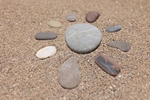 Figure of sun is made of pebble stones on sandy beach in summer