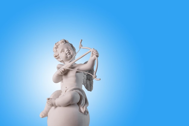 Figurine of an angel Cupid on the podium with a bow and arrow on a blu background Valentine's DayPlace for text