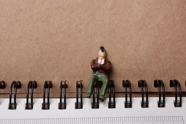 The figurine of a little man sitting beside spiral notebook