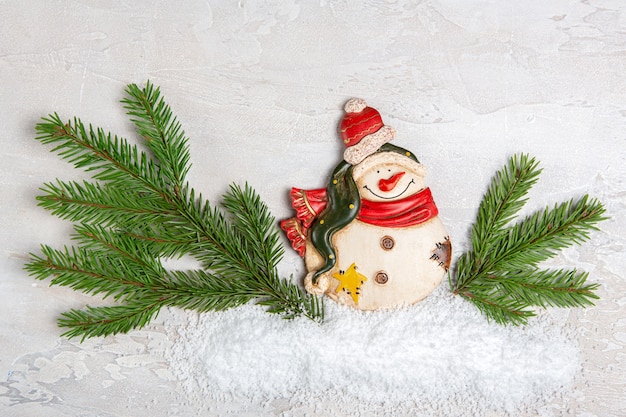 A figurine of a snowman with spruce branches on a light concrete