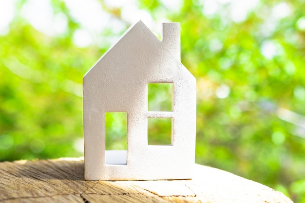 Figurine of a white ceramic house on a wooden surface against the background of green trees