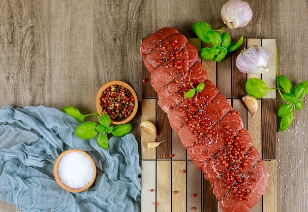 Filet mignon, prepared marinade for roast with garlic, peppercorns, herbs, and spices ready for cooking on a wooden board.